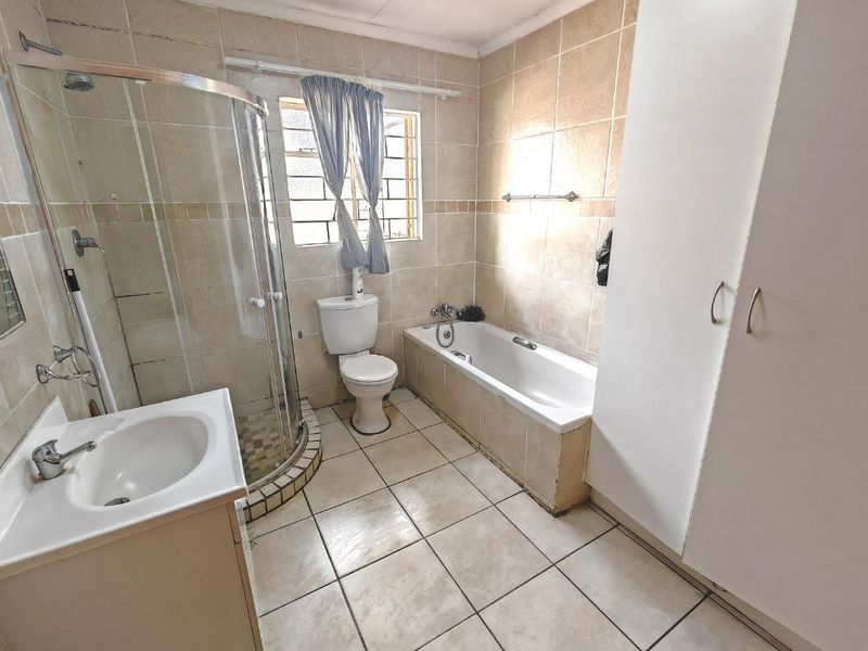 A functional bathroom featuring a shower enclosure, bathtub, toilet, vanity basin, and built-in storage cupboard with neutral tiled finishes.