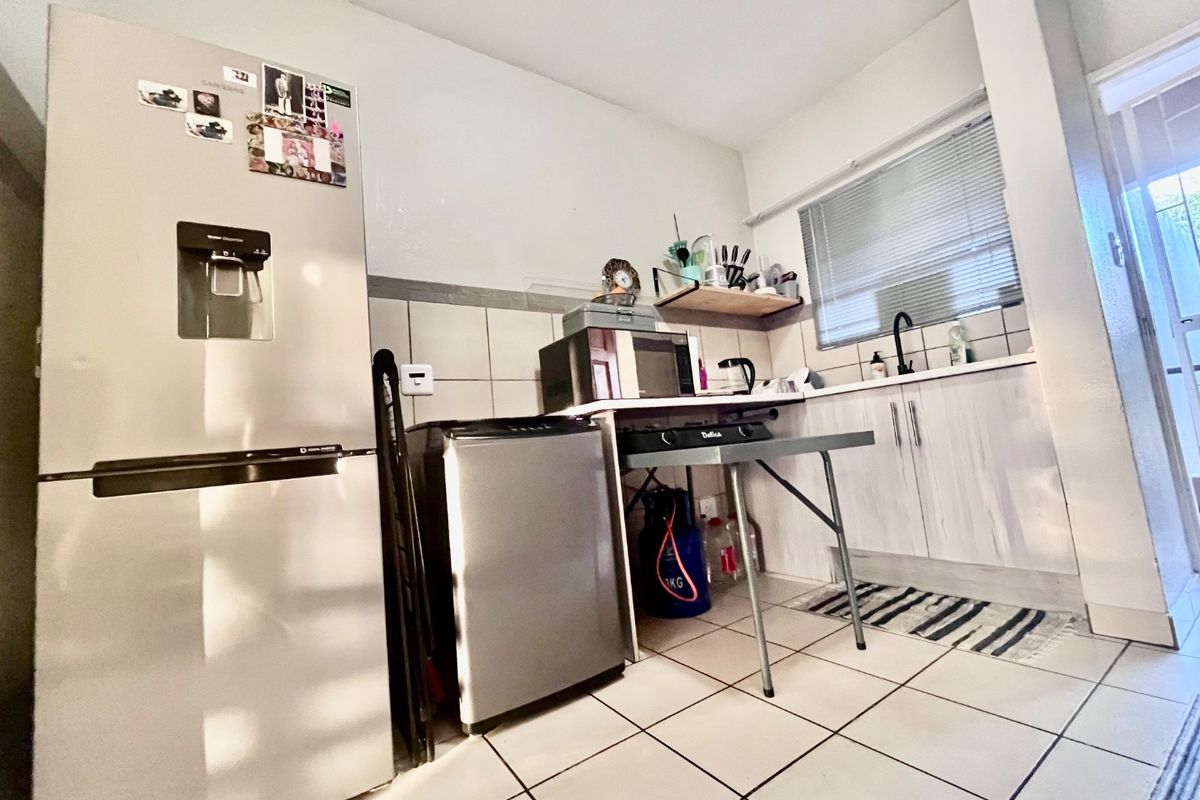 A compact kitchen area featuring tiled flooring, a tiled backsplash, and basic cabinetry with a sink, requiring modernization of fixtures and finishes.