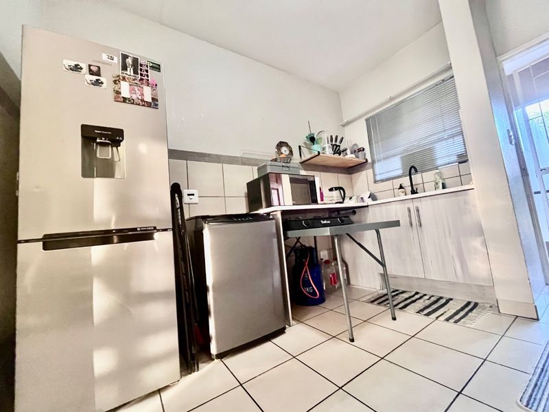 A compact kitchen area featuring tiled flooring, a tiled backsplash, and basic cabinetry with a sink, requiring modernization of fixtures and finishes.