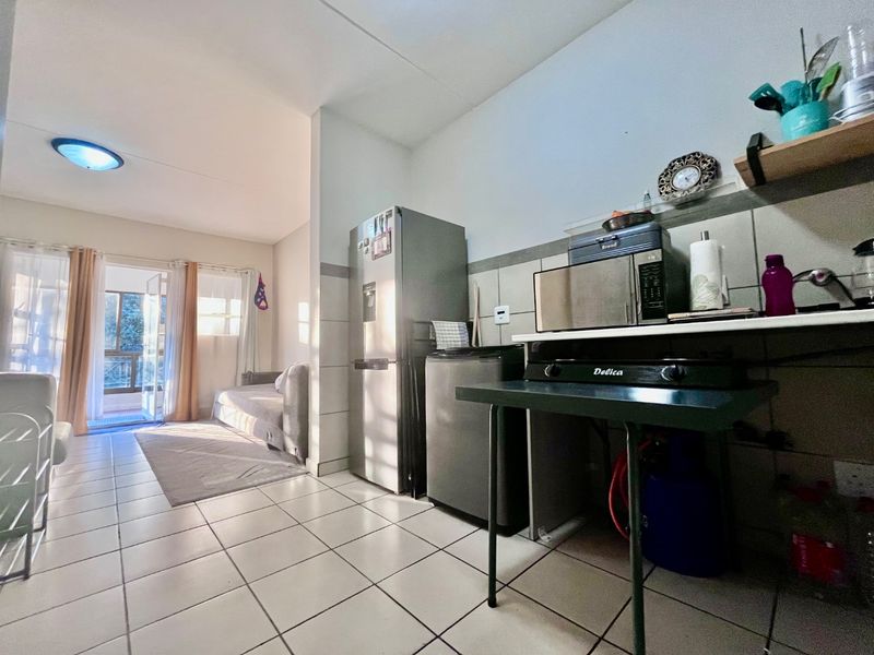 Open plan living area featuring tiled flooring and a functional kitchen space with direct access to a balcony through a sliding door.