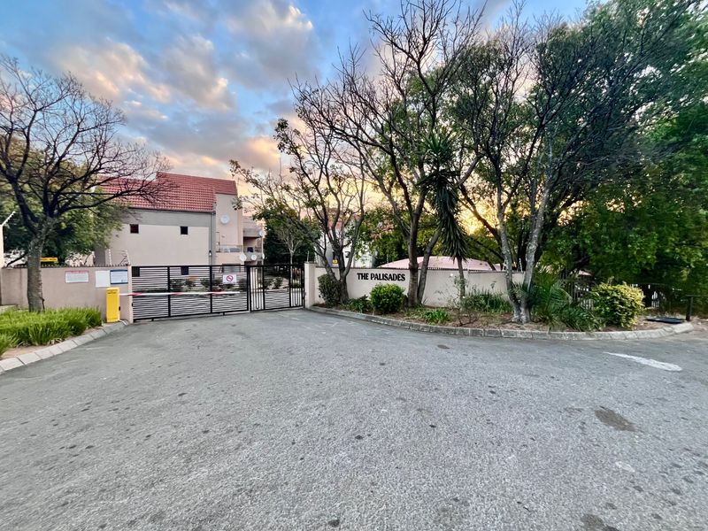 The entrance to The Palisades apartment complex, featuring a secure gated access point, boom gate, and perimeter wall with electric fencing.