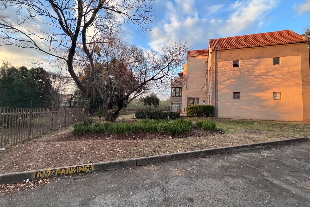 Rear view of the apartment complex featuring a tiled roof, landscaped garden beds, and secure perimeter fencing.