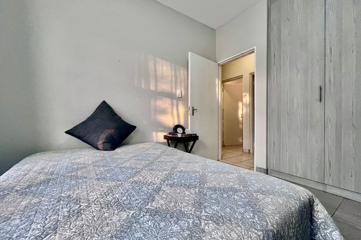 A well-maintained bedroom featuring built-in wardrobes, neutral wall finishes, and tiled flooring, with an adjoining hallway visible through the doorway.