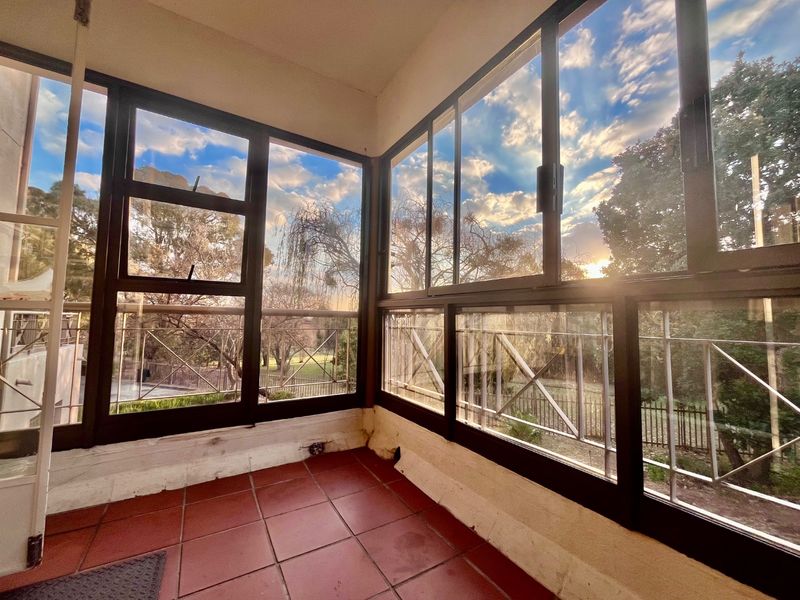 Enclosed balcony featuring tiled flooring and large aluminium-framed windows with views of the surrounding greenery.