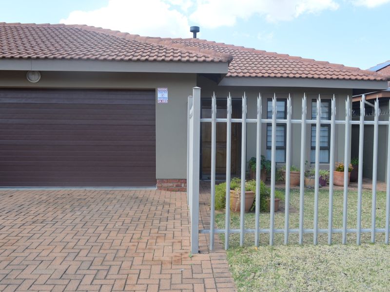 Front elevation of a townhouse featuring a paved driveway, single sectional garage door, and secure steel perimeter fencing.