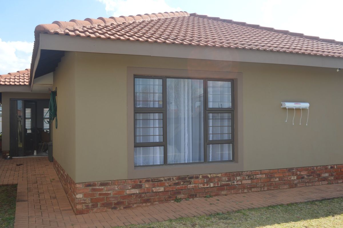 Rear exterior view of the townhouse featuring a tiled roof, brick base detailing, aluminium window frames with security bars, and a paved walkway.