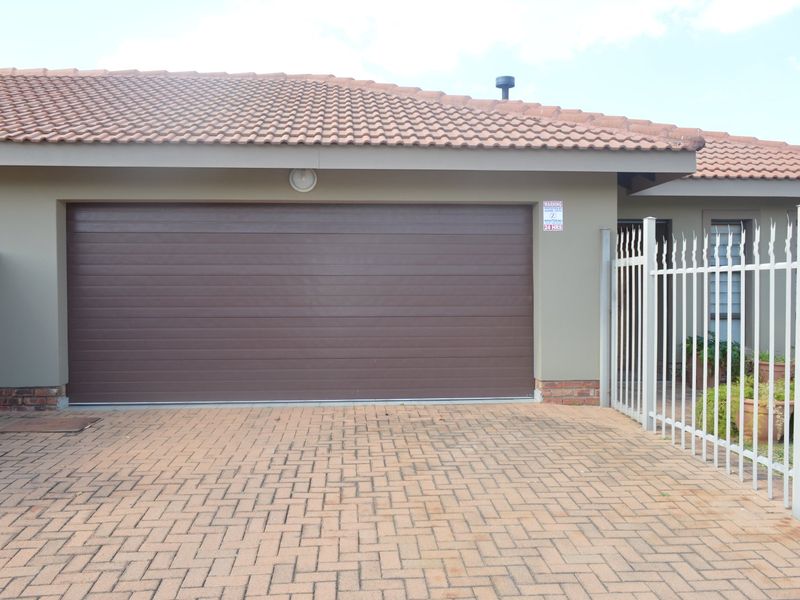 A well-maintained townhouse exterior featuring a brown sectional garage door, paved driveway, and secure metal fencing.