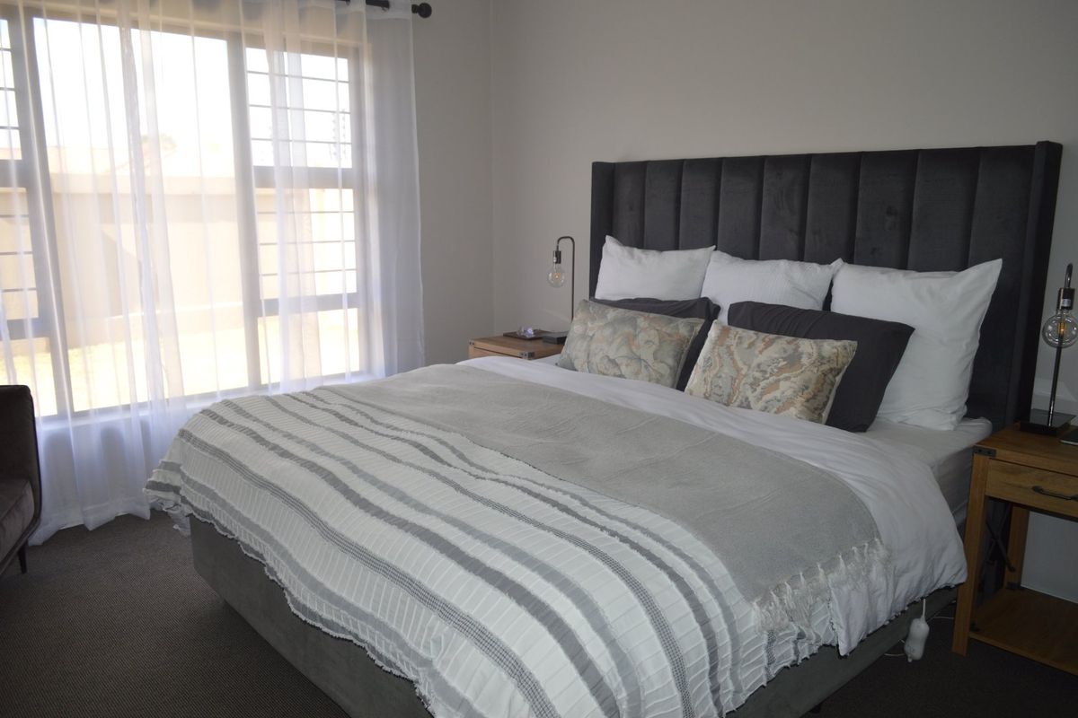 A well-maintained bedroom featuring carpeted flooring and a large window fitted with security bars, providing natural light.