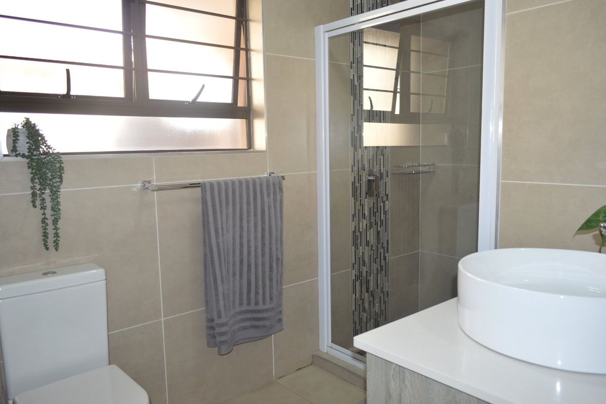 Modern bathroom featuring a glass-enclosed shower, neutral wall tiling, a contemporary vessel sink vanity, and a window with security bars.