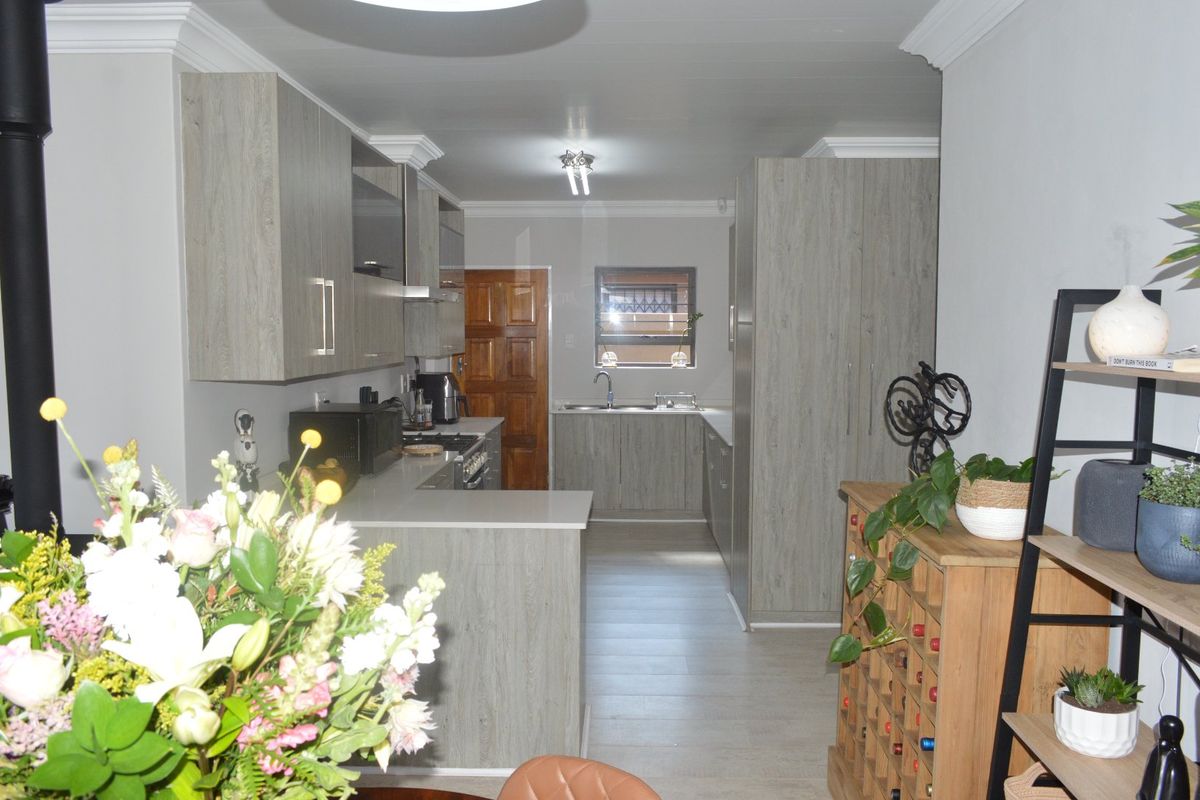 A modern kitchen featuring light wood-grain cabinetry, stone countertops, integrated appliances, and a functional layout with a breakfast bar area.