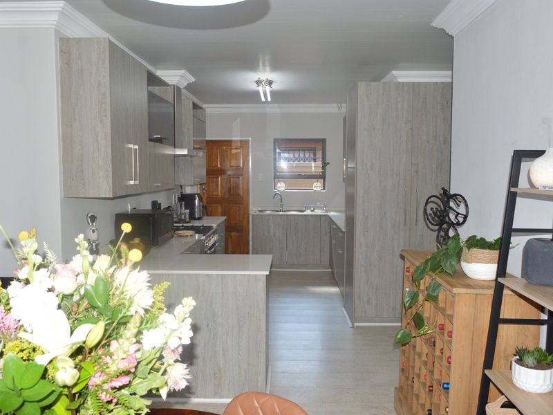 A modern kitchen featuring light wood-grain cabinetry, stone countertops, integrated appliances, and a functional layout with a breakfast bar area.