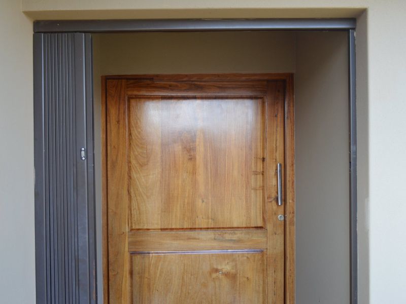 A solid wood front door featuring a modern handle, set within a neutral-toned entrance frame with an integrated security gate track.