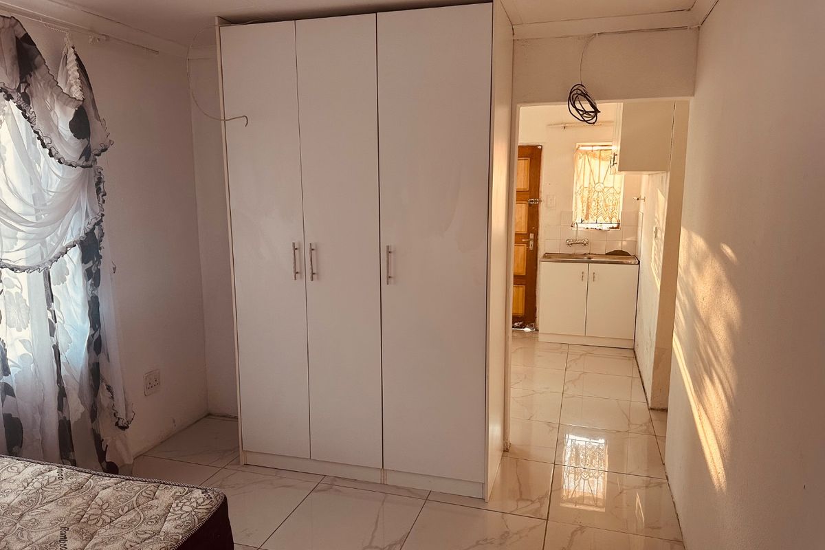 Bedroom featuring tiled flooring and a built-in wardrobe, with an adjacent kitchenette area visible through the doorway.
