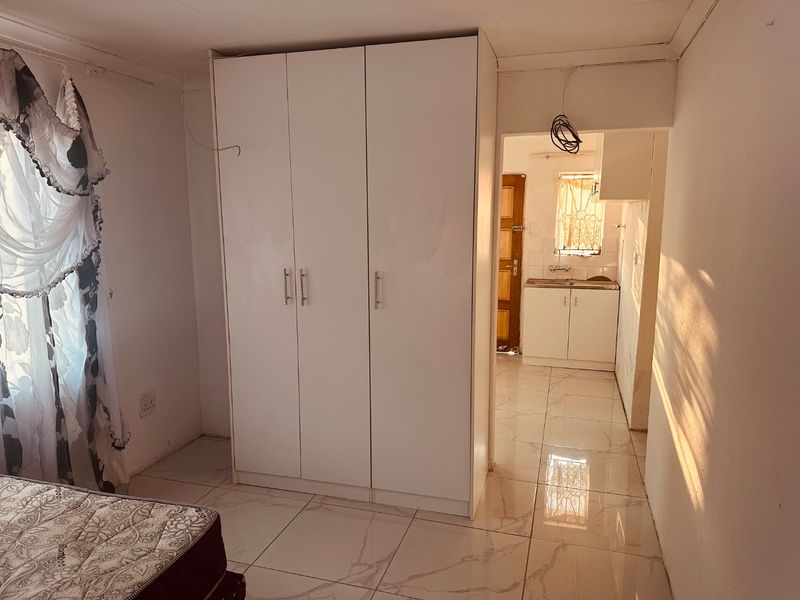 Bedroom featuring tiled flooring and a built-in wardrobe, with an adjacent kitchenette area visible through the doorway.