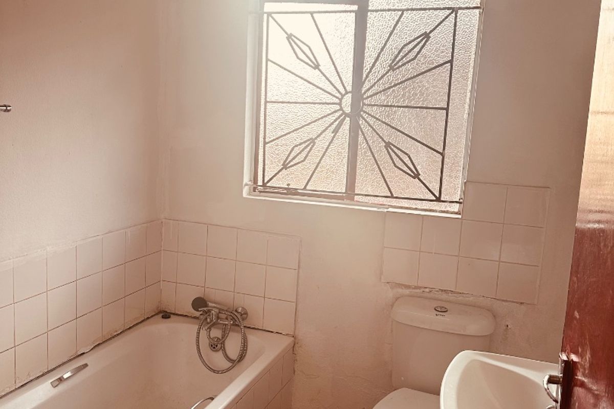 A functional bathroom featuring a bathtub, toilet, and wall-mounted basin, with tiled splashbacks and a security-fitted window.