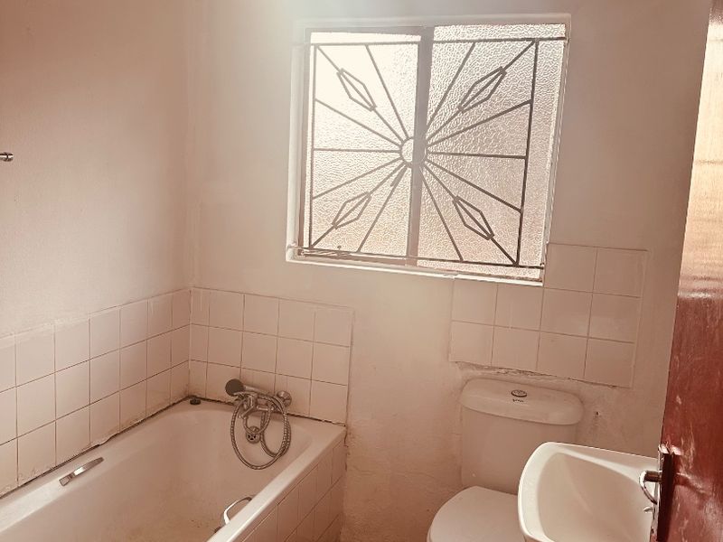 A functional bathroom featuring a bathtub, toilet, and wall-mounted basin, with tiled splashbacks and a security-fitted window.