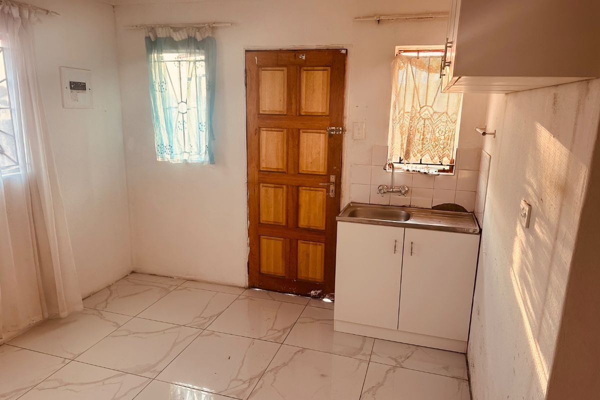 A compact kitchen area featuring tiled flooring, a stainless steel sink with base cabinetry, and a timber entrance door.