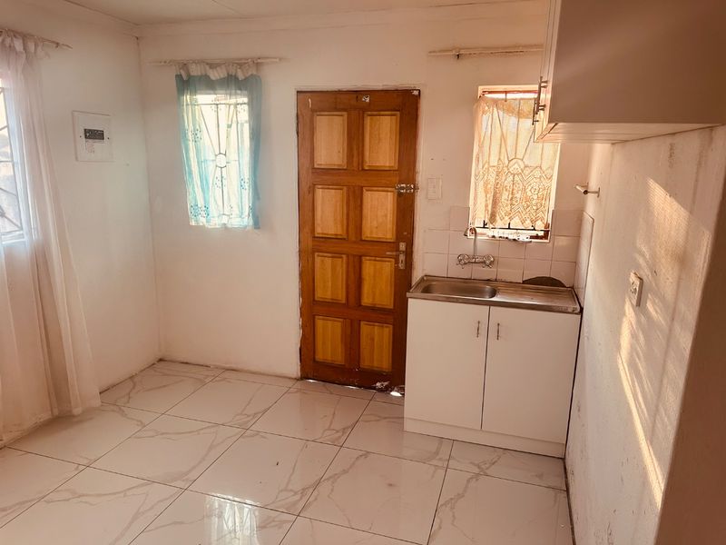 A compact kitchen area featuring tiled flooring, a stainless steel sink with base cabinetry, and a timber entrance door.
