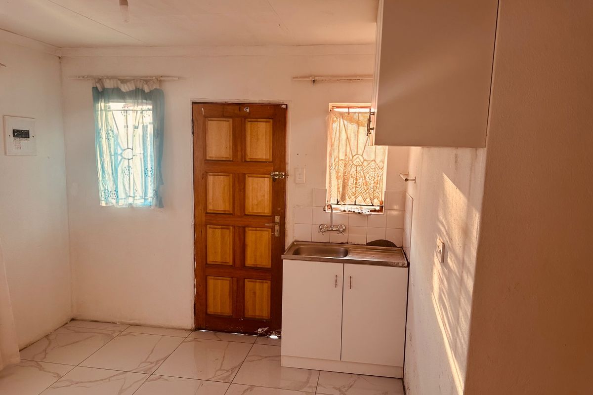 A compact kitchen area featuring tiled flooring, a single stainless steel sink with base and wall cabinetry, and direct access to an exterior door.