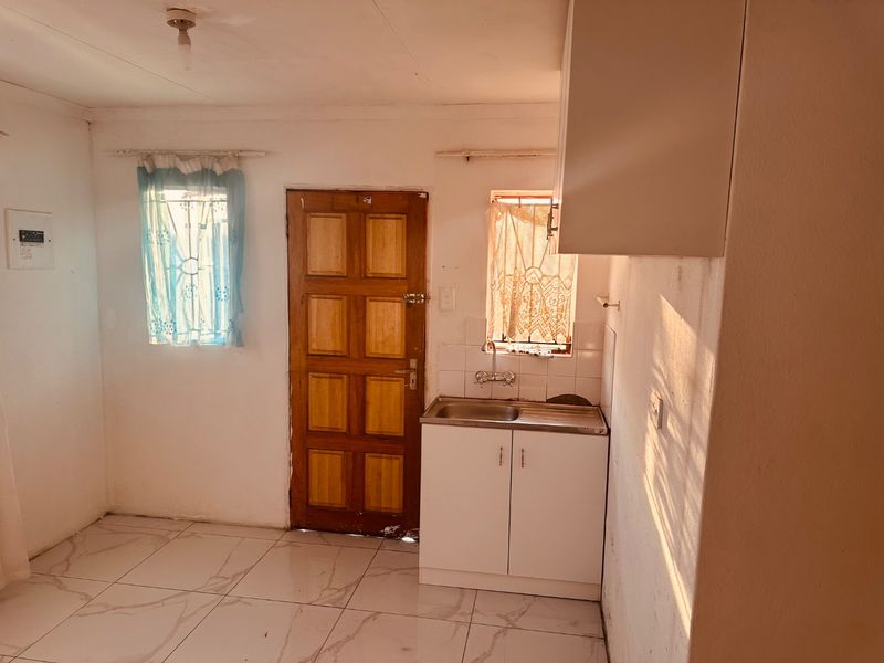 A compact kitchen area featuring tiled flooring, a single stainless steel sink with base and wall cabinetry, and direct access to an exterior door.