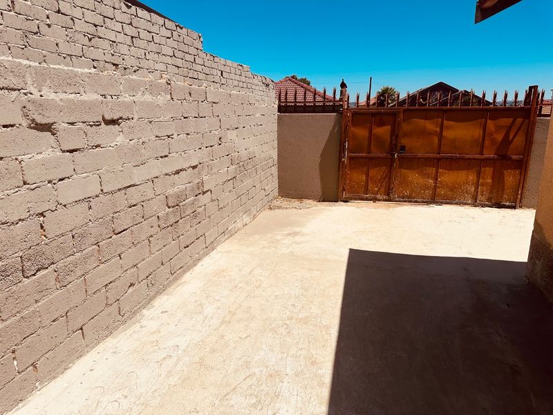 A private rear courtyard area featuring a concrete boundary wall and a metal gate, offering a blank canvas for outdoor improvement.