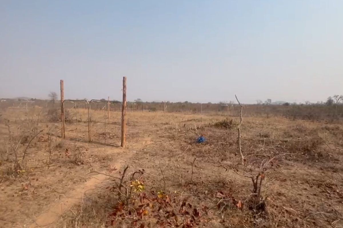 A view of a vacant residential plot featuring dry vegetation, wire perimeter fencing, and basic wooden fence posts.