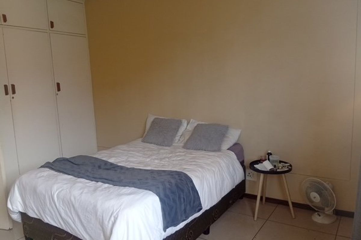 A functional bedroom featuring neutral wall tones, tiled flooring, and ample built-in cupboard storage space.