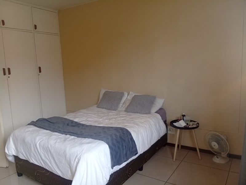 A functional bedroom featuring neutral wall tones, tiled flooring, and ample built-in cupboard storage space.