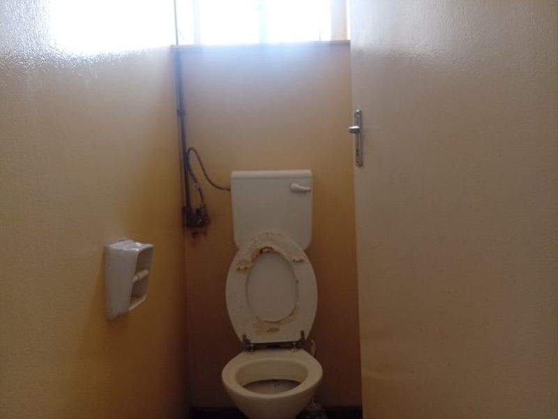 A small, dated bathroom featuring a standard toilet with visible plumbing and a wall-mounted toilet roll holder.