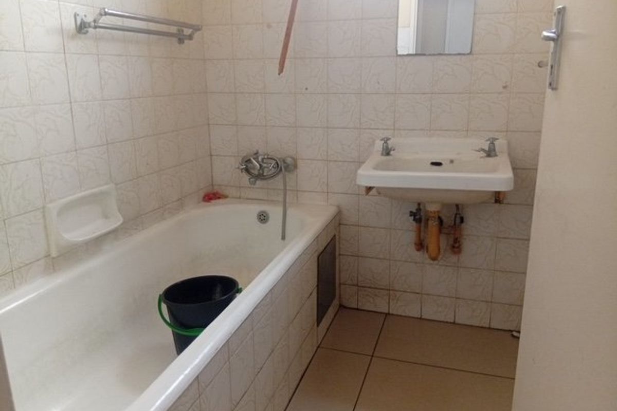 A dated bathroom featuring a standard bathtub, wall-mounted basin, and tiled finishes, offering potential for modernization and renovation.