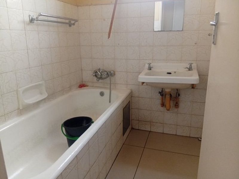 A dated bathroom featuring a standard bathtub, wall-mounted basin, and tiled finishes, offering potential for modernization and renovation.