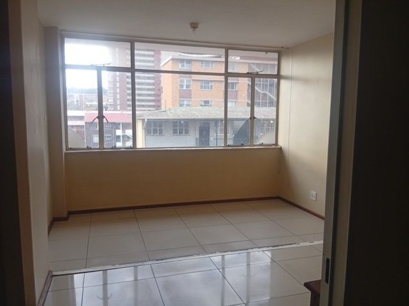 An empty, sunlit living area featuring large aluminium-framed windows and neutral tiled flooring, offering a blank canvas for interior design.