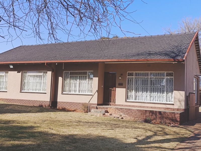 Front view of a single-story residential house featuring a tiled roof, brick base, paved driveway, and a detached garage.