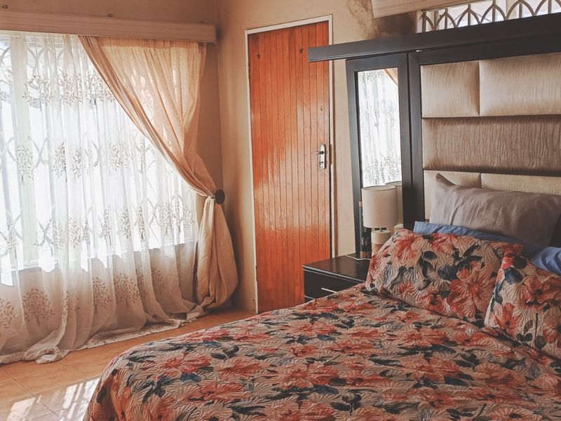 A bedroom featuring tiled flooring, a wooden door, and a security gate over the window, showing signs of wear near the door frame.