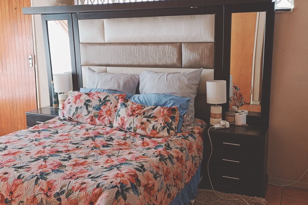 A bedroom featuring a built-in headboard, tiled flooring, and a wooden door, with some visible wear on the wall finishes.