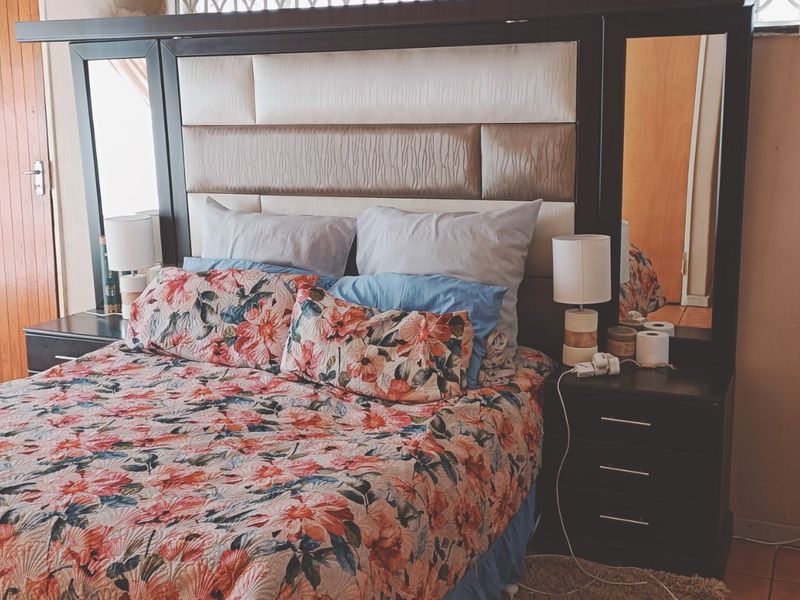 A bedroom featuring a built-in headboard, tiled flooring, and a wooden door, with some visible wear on the wall finishes.