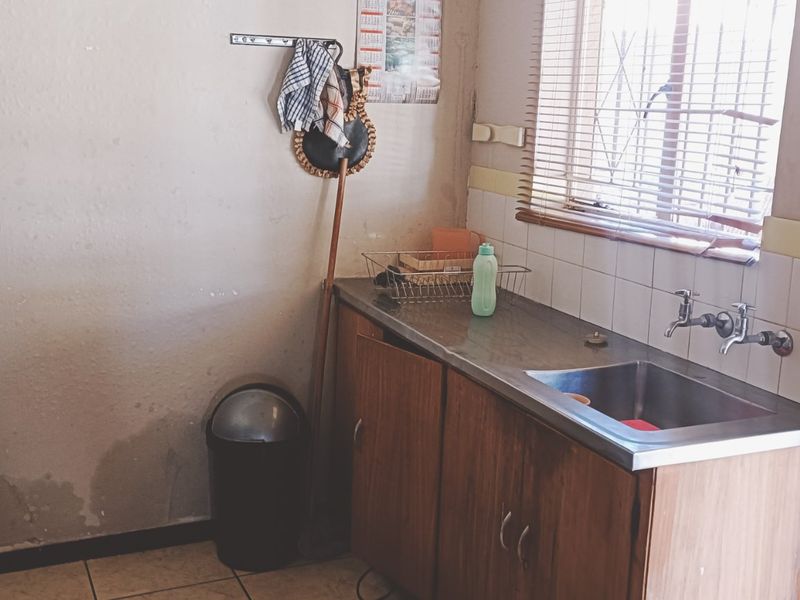 A functional laundry area featuring a stainless steel sink, built-in cabinetry, and tiled splashback, requiring some cosmetic wall repairs.