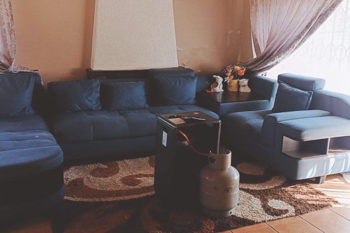 A living room featuring tiled flooring and a central fireplace, showing signs of wear on the wall finish.