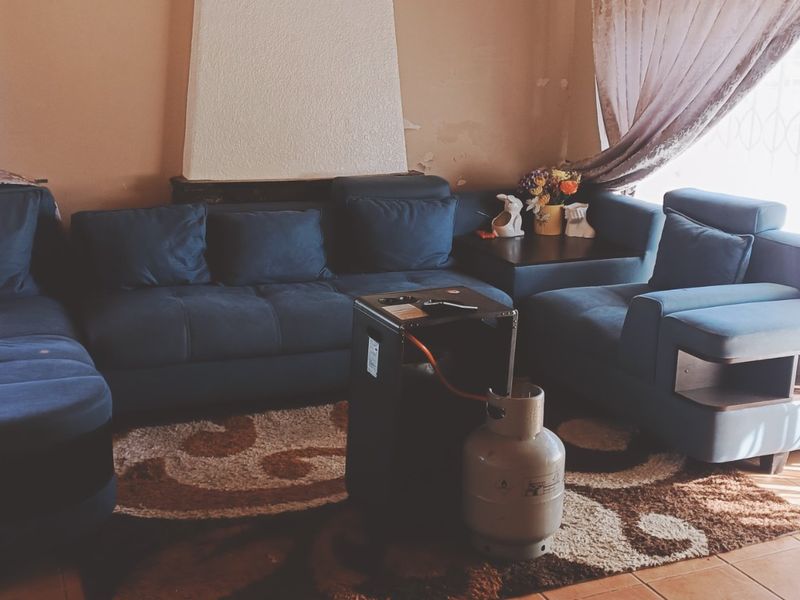 A living room featuring tiled flooring and a central fireplace, showing signs of wear on the wall finish.