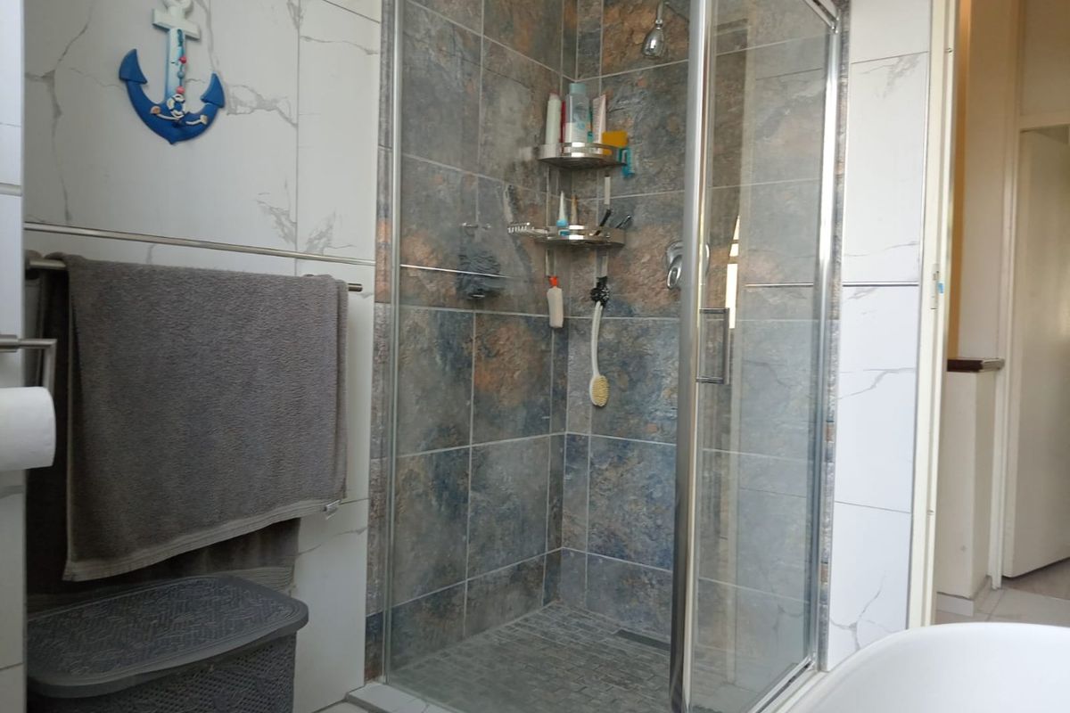A functional bathroom featuring a glass-enclosed shower with textured wall tiling and neutral floor tiles.