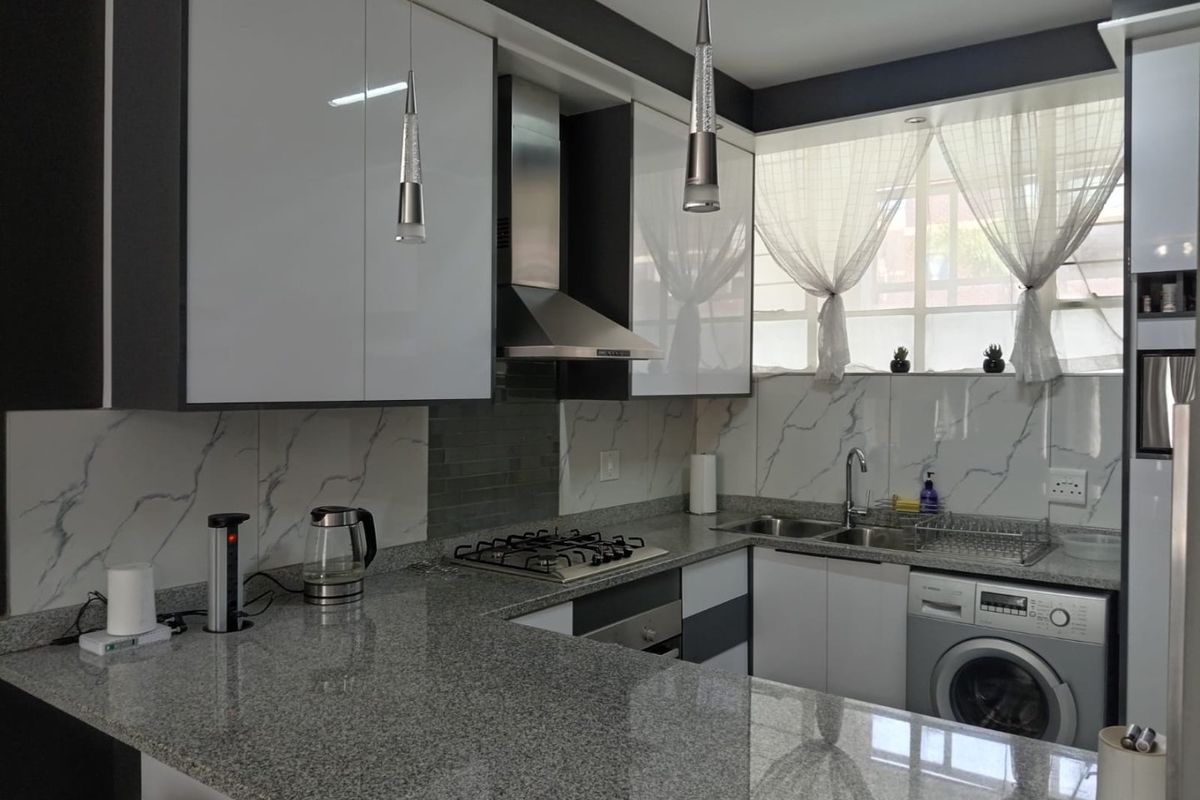 Modern kitchen featuring high-gloss cabinetry, granite countertops, a built-in gas hob, stainless steel extractor, and integrated washing machine.