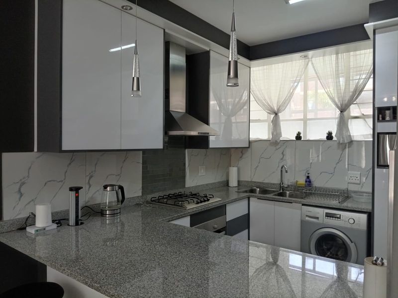 Modern kitchen featuring high-gloss cabinetry, granite countertops, a built-in gas hob, stainless steel extractor, and integrated washing machine.