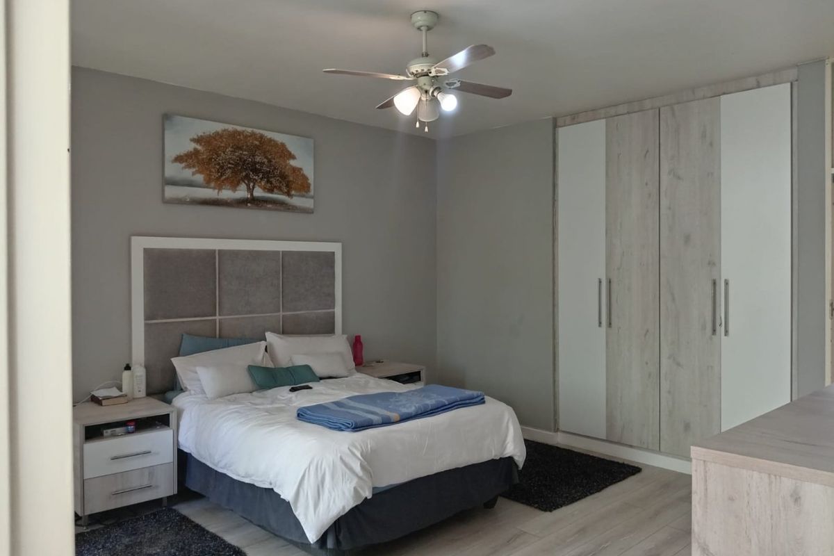 A well-maintained bedroom featuring light-toned laminate flooring, a ceiling fan, and modern built-in cupboards with a neutral color palette.
