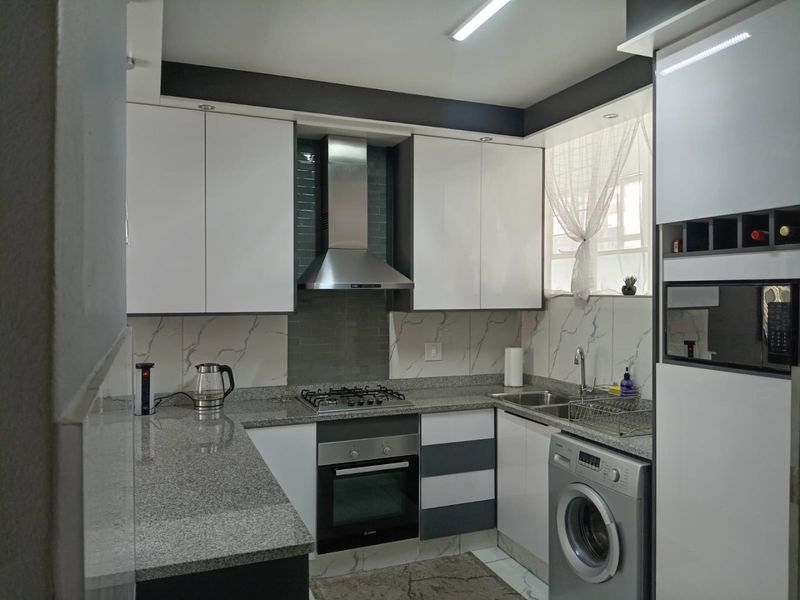 Modern kitchen featuring granite countertops, built-in oven, gas hob, stainless steel extractor fan, and ample cabinetry with a clean, contemporary finish.