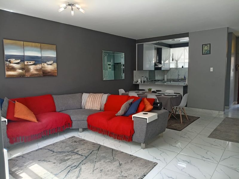 Open-plan living and dining area featuring modern marble-look floor tiles and a compact, functional kitchen with integrated cabinetry and breakfast counter.