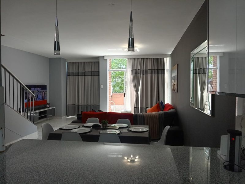 Spacious open-plan living and dining area featuring modern pendant lighting, tiled floors, and a staircase, with direct access to a balcony.