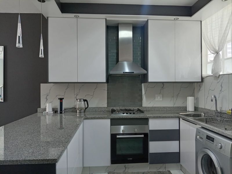 Modern kitchen featuring granite countertops, marble-look splashbacks, built-in oven, gas hob, and stainless steel extractor fan with ample cabinetry.