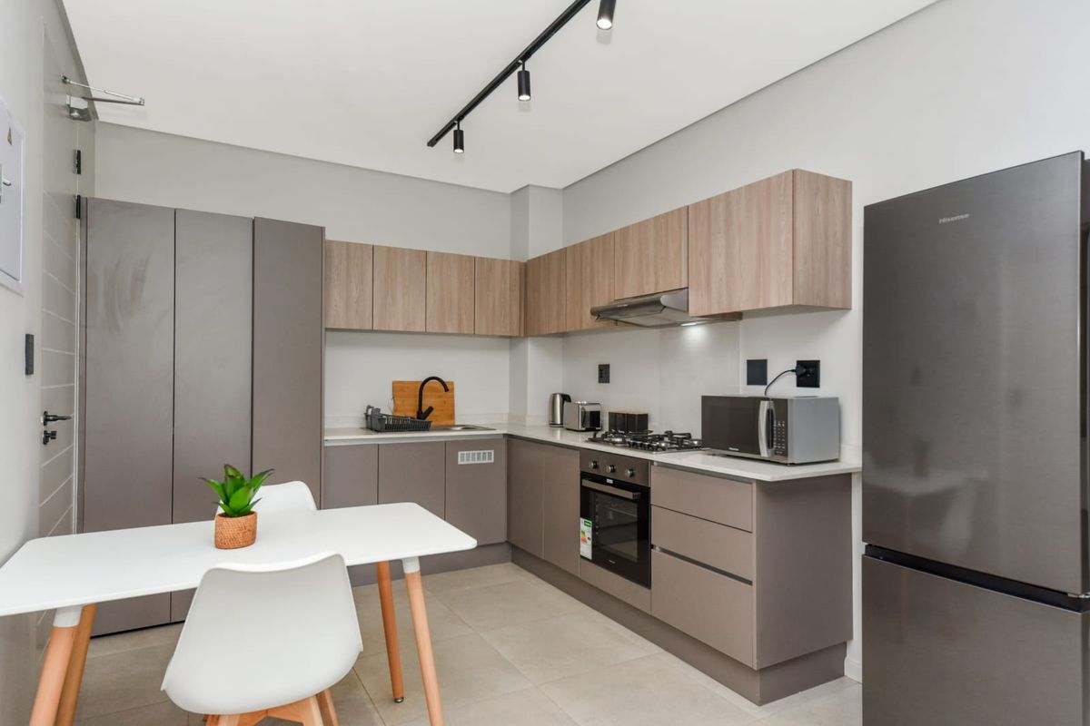 Modern kitchen featuring sleek cabinetry, stone countertops, integrated gas hob, electric oven, and contemporary track lighting in a clean, well-maintained space.