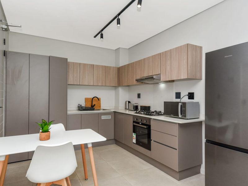 Modern kitchen featuring sleek cabinetry, stone countertops, integrated gas hob, electric oven, and contemporary track lighting in a clean, well-maintained space.