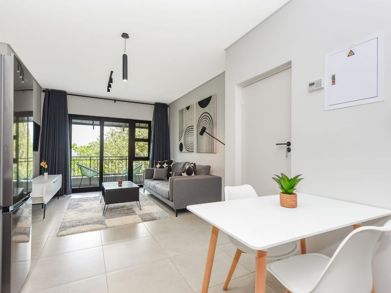 Modern open-plan living area featuring neutral tiled flooring, track lighting, and a sliding glass door leading to a private balcony.